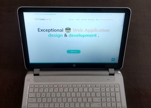 A laptop computer with a website displayed on the screen featuring the text 'Exceptional Web Application design & development'. The laptop is on a dark surface, and the website has a clean and modern design with a light background and colorful text elements.