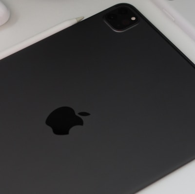 A close-up view of technology devices including a black tablet with a prominent logo, a white smartphone, a camera lens, and a stylus on a white surface.