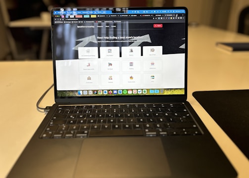 A laptop displaying a website with a search bar at the top and several categorized icons for different services. The laptop is positioned on a light-colored desk in an indoor setting, with the focus on the screen contents and some blurred background elements.